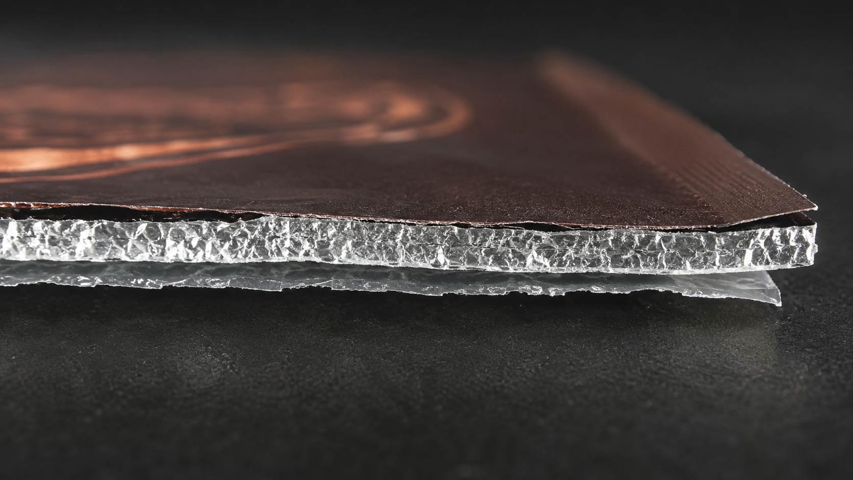 Close-up cutaway of a coffee bag wall showing the layered barrier film, with the aluminum layer visible between the printed outer layer and the inner sealant