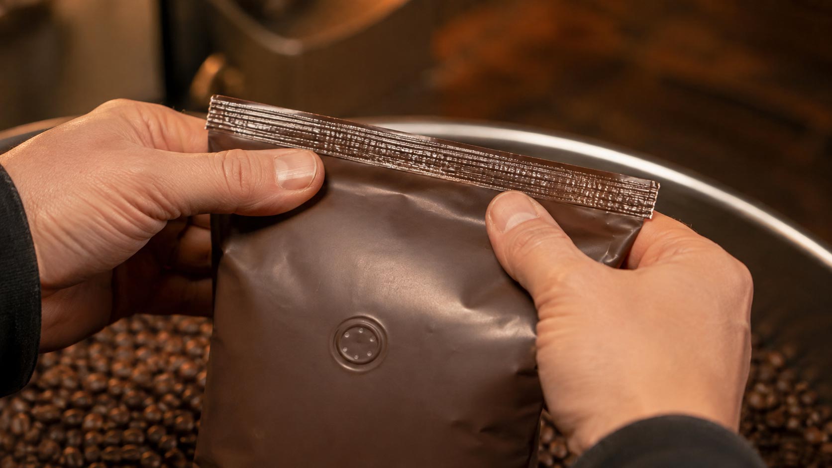 A roaster holding a filled coffee bag up to the light to inspect the top seal after filling