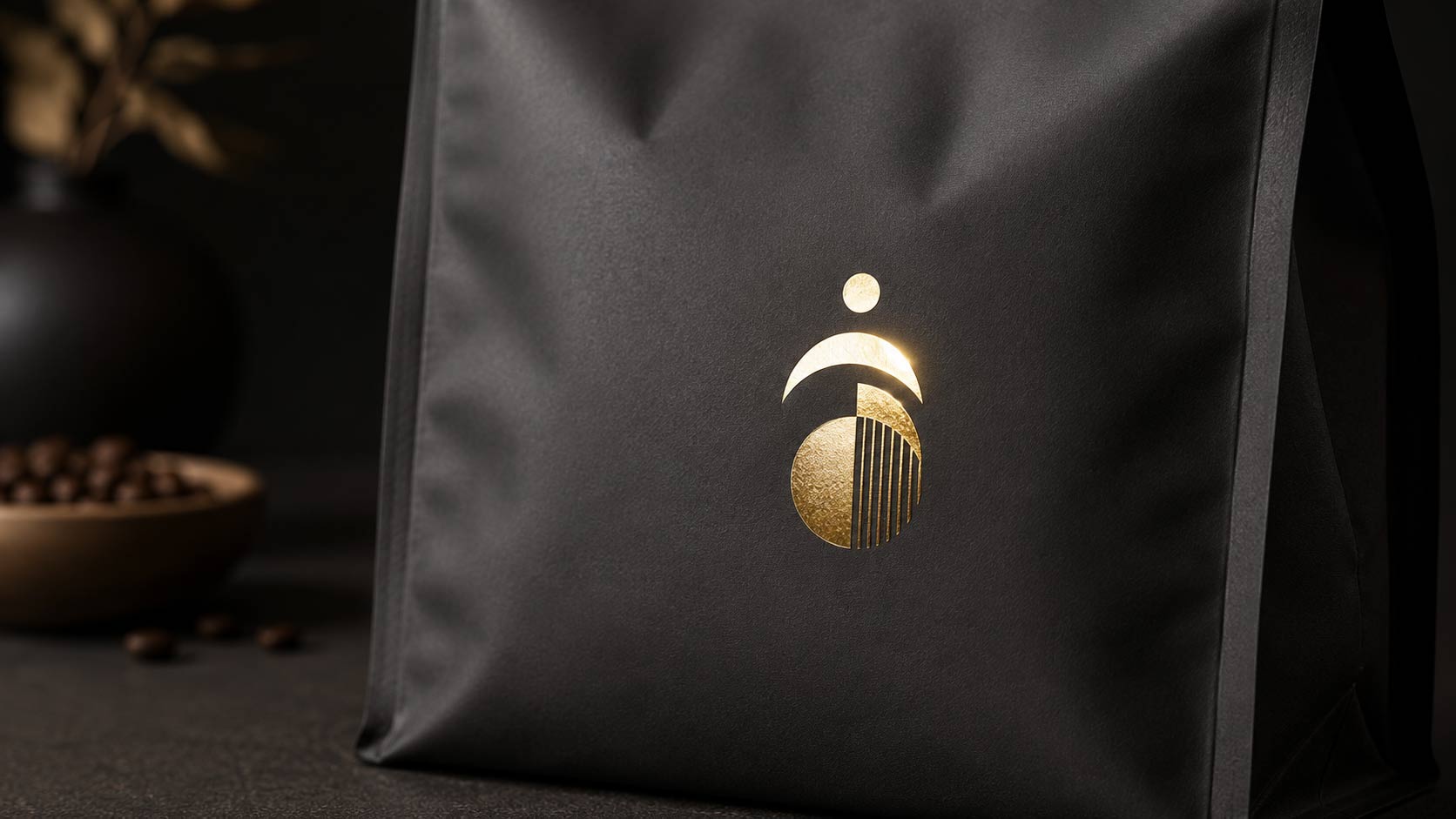 Close-up of a small gold foil stamped logo reflecting a bright highlight on a dark matte coffee bag