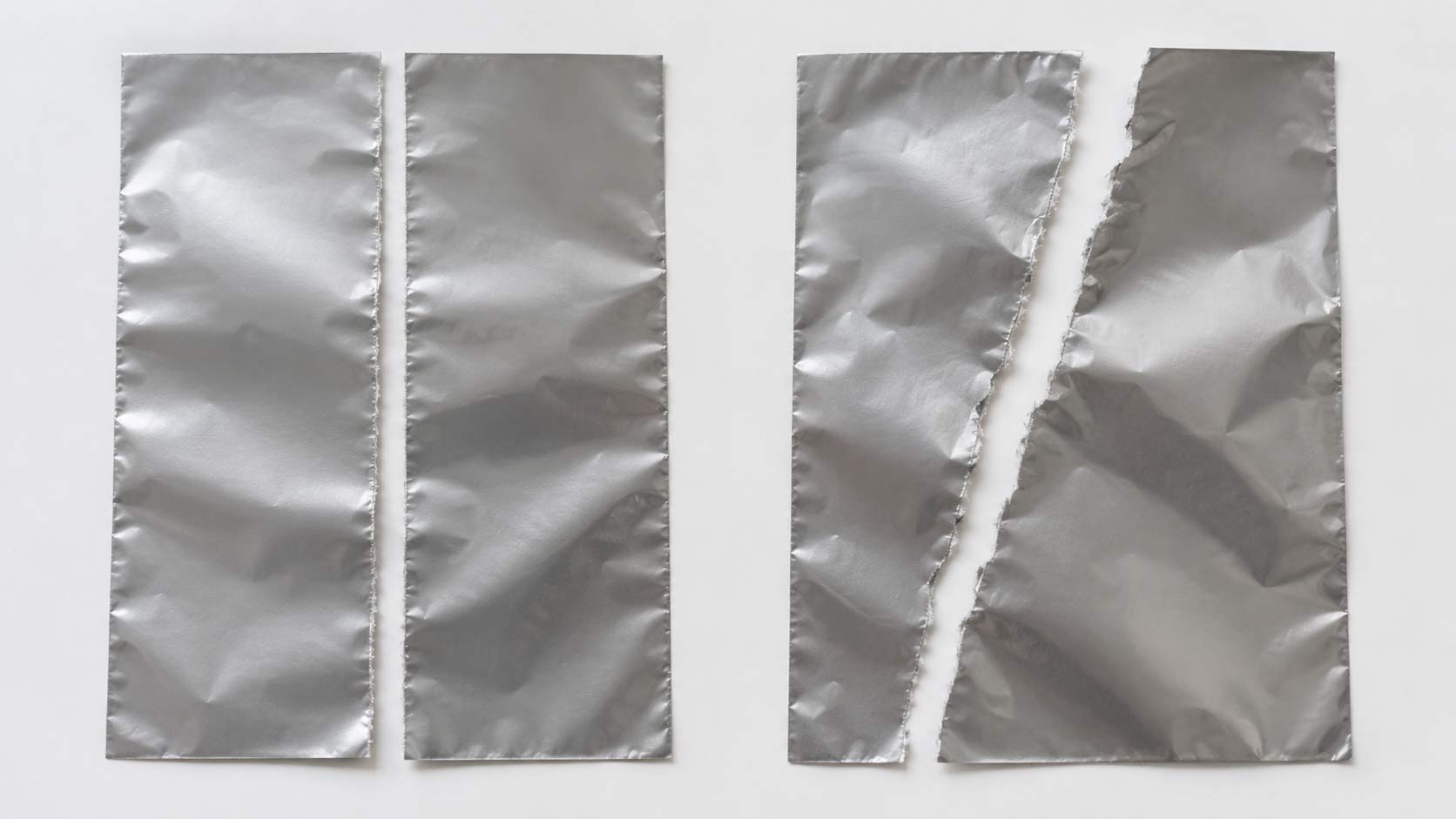 Two strips of packaging film torn by hand, one tearing in a straight line along the grain and the other wandering off at an angle across it