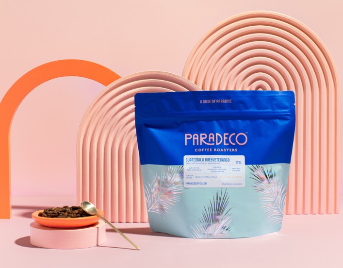 Blue coffee bag with shiny holographic palm leaves on pink background with pink coffee cup